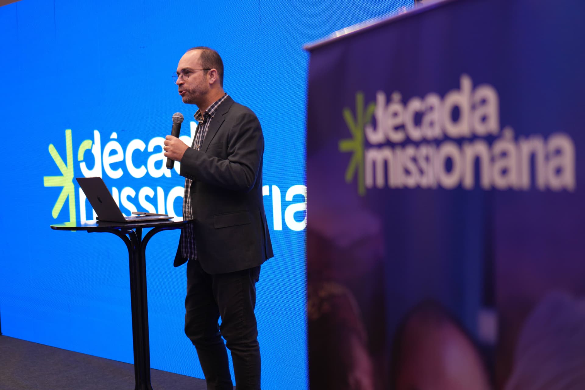 Palestrante com microfone diante da identidade Década Missionária
