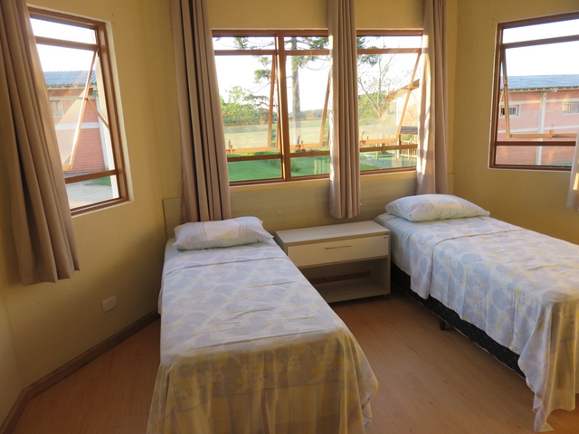 Quarto com duas camas e janelas voltadas ao jardim